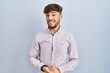 © Krakenimages.com - Arab man with beard standing over blue background with hands together and crossed fingers smiling relaxed and cheerful. success and optimistic