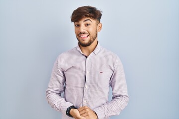 Poster - Arab man with beard standing over blue background with hands together and crossed fingers smiling relaxed and cheerful. success and optimistic