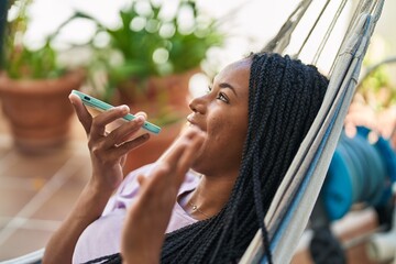 Poster - African american woman talking on smartphone lying on hammock at home terrace