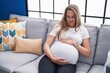 Young pregnant woman touching belly sitting on sofa at home