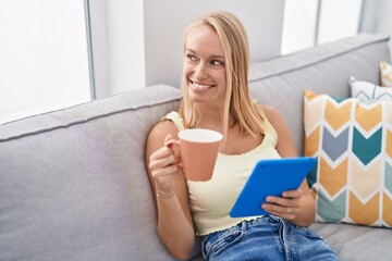 Poster - Young blonde woman drinking coffee and using touchpad at home