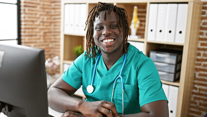 Wall Mural - African american man doctor using computer smiling at the clinic