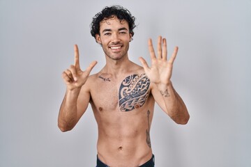 Canvas Print - Hispanic man standing shirtless showing and pointing up with fingers number seven while smiling confident and happy.