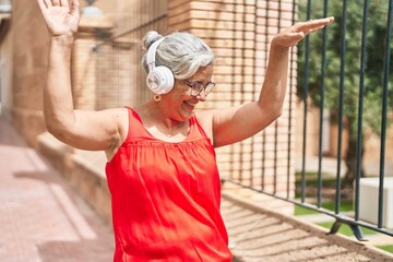 Wall Mural - Middle age grey-haired woman listening to music and dancing at street