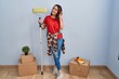 © Krakenimages.com - Young hispanic woman painting home walls with paint roller smiling with hand over ear listening an hearing to rumor or gossip. deafness concept.