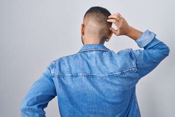 Wall Mural - Young hispanic man standing over isolated background backwards thinking about doubt with hand on head