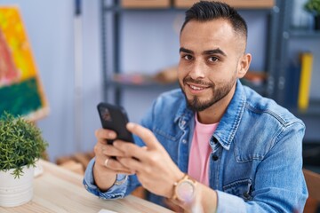 Wall Mural - Young hispanic man artist using smartphone drawing at art studio