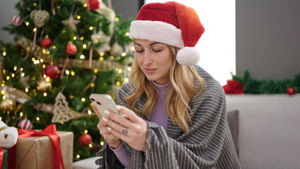 Wall Mural - Young beautiful hispanic woman using smartphone celebrating christmas at home