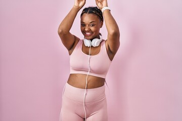 Poster - African american woman with braids wearing sportswear and headphones posing funny and crazy with fingers on head as bunny ears, smiling cheerful