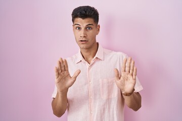 Sticker - Young hispanic man standing over pink background moving away hands palms showing refusal and denial with afraid and disgusting expression. stop and forbidden.