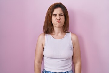 Sticker - Brunette woman standing over pink background puffing cheeks with funny face. mouth inflated with air, crazy expression.