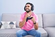 © Krakenimages.com - Hispanic young man playing video game holding controller sitting on the sofa touching painful neck, sore throat for flu, clod and infection