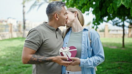 Poster - Man and woman couple holding heart package gift kissing at park