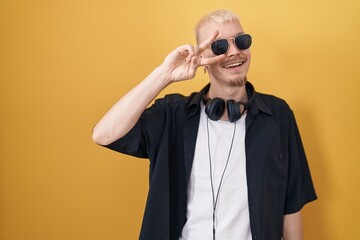 Poster - Young caucasian man wearing sunglasses standing over yellow background doing peace symbol with fingers over face, smiling cheerful showing victory