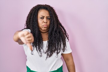 Wall Mural - Plus size hispanic woman standing over pink background looking unhappy and angry showing rejection and negative with thumbs down gesture. bad expression.