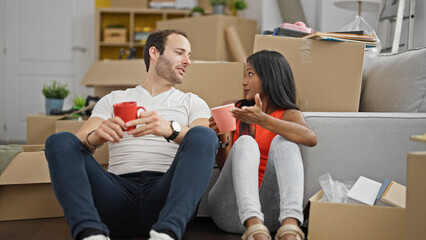 Wall Mural - Beautiful couple sitting on floor together drinking coffee speaking at new home