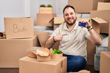 Wall Mural - Plus size hispanic man with beard moving to a new home holding credit card pointing finger to one self smiling happy and proud