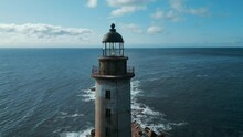 Top View Of Abandoned Lighthouse In Sea On Sunny Day. Clip. Abandoned Lighthouse On Rocks With Waves Of Blue Sea. Beautiful Lighthouse On Background Of Sea Waves Crashing On Rocks