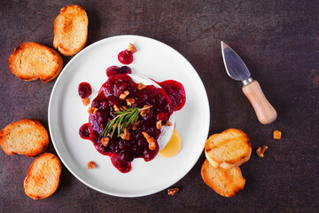 Poster - Baked brie appetizer garnished with cranberry sauce and walnuts. Top down view table scene with toasted baguette over a dark background.