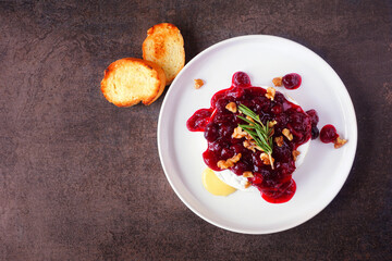 Poster - Baked brie appetizer garnished with cranberry sauce and walnuts. Overhead view on a dark background.