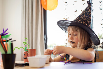 Wall Mural - A cute girl in a witch costume makes a funny spider for Halloween with her own hands. Children's crafts for Halloween