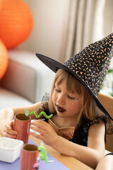 Wall Mural - A cute girl in a witch costume makes a paper craft for Halloween. Children's crafts for Halloween.