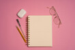 Top view image of open notebook with blank pages. work notebook on a pink background, spiral notepad on a table with glasses and pencils