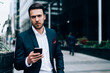© BullRun - Serious businessman using smartphone on street