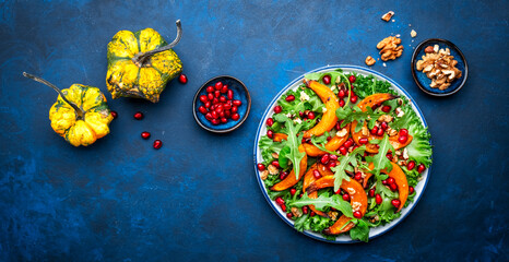Wall Mural - Vegan autumn salad with baked sweet pumpkin, lettuce, arugula, pomegranate seeds and walnuts. Comfort slow  food. Blue background. Top view