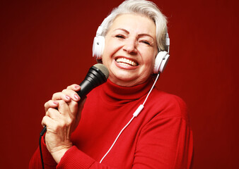 Happy old woman singing with microphone, having fun, expressing musical talent over red background