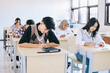 © Gatot - Group of high school students sitting in classroom and writing in notebooks.