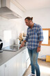 © Taras Grebinets - Full length portrait of a handsome Caucasian man in casual clothes switching on an electric stove in the home kitchen