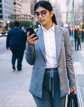 Confident young formal pretty business lady surfing smartphone on street