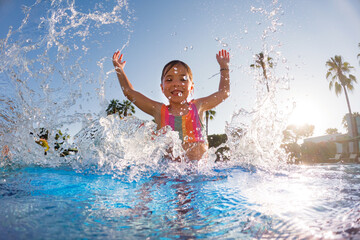 Little girl splashing water in the pool, playing in the water, having fun. Beach resort vacation by sea. Winter or summer seaside resort holiday.