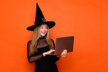 Sticker - Photo of cute excited girl dressed dark witch dress headwear texting emails modern device empty space isolated orange color background