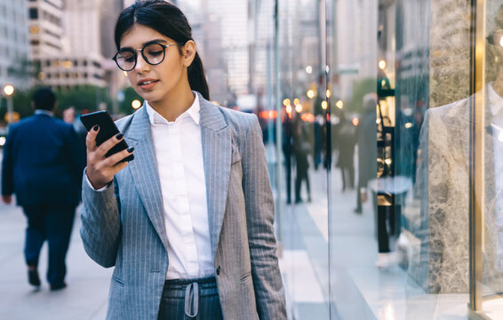 Confident young formal pretty business lady surfing smartphone on street