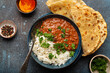 Traditional Indian Punjabi dish Dal makhani with lentils and beans in black bowl served with basmati rice, naan flat bread, fresh cilantro and spoon on blue concrete rustic table top view.