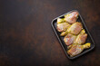 Raw uncooked chicken legs in green marinade with seasonings in black plastic container top view on dark rustic background. Preparing healthy meal with marinated chicken drumsticks, copy space.