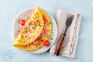 An omelet with tomato and parsley, eggs for breakfast, a healthy vegetarian dish with cheese, overhead flat lay shot with a fork