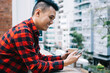 © BullRun - Joyful youthful Asian male having fun with cellphone on balcony