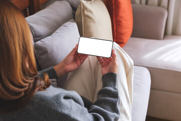 Poster - Mockup image of a woman holding mobile phone with blank desktop white screen while lying on a sofa at home