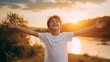 Boy kid wearing a white t-shirt joyfully raises his arms, his vibrant energy shining against a captivating nature landscape at sunset , portraying an aura of positivity and exuberance