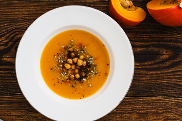 Wall Mural - Bowl with vegan pumpkin and chickpea cream soup  on wooden table, directly above