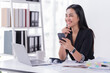 © Tj - Sharing good business news. Attractive young businesswoman talking on the mobile phone and smiling while sitting at her working place in office and looking at laptop PC.