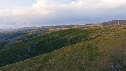 Wall Mural - The hilly country of Croatia with grassland and tress. Some wind turbines spin in the wind. Drone move forward