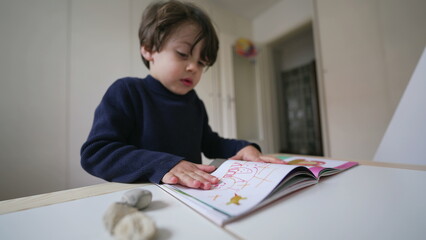 Wall Mural - Child turning book pages looking at images and text. Little boy reading kindergarten school material