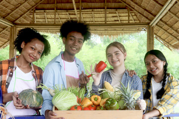 Wall Mural - Group of happy Multiethnic teenager friend holding organic food products from their own farm at local market fair, smiling young diverse farmer selling fresh harvest fruit and vegetable at marketplace