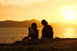 © Dmytrii - Silhouette of girl admiring beautiful sunset sitting on stone on sea coast. Silhouette of a man and a woman sitting on the seashore at sunset