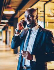 Wall Mural - Cheerful black businessman speaking on smartphone in office hallway