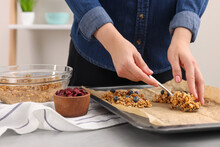 Making Granola Bars. Woman Putting Mixture Of Oat Flakes, Dry Fruits And Other Ingredients Onto Baking Tray At Table In Kitchen, Closeup